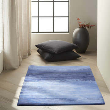 Minimalist room with a Calvin Klein Home Luster Wash Indigo rug, gray pillows, and a black vase.