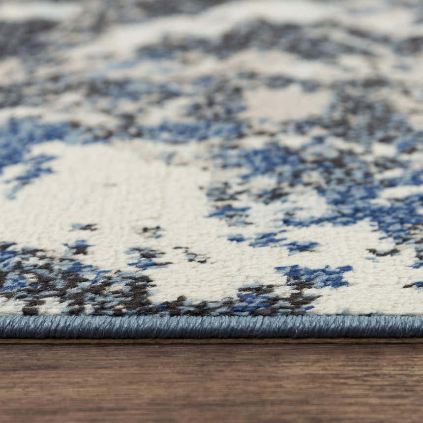 Close-up of Rizzy PLC855 area rug showing abstract pattern in beige, black, and blue on a textured polypropylene surface. Pile