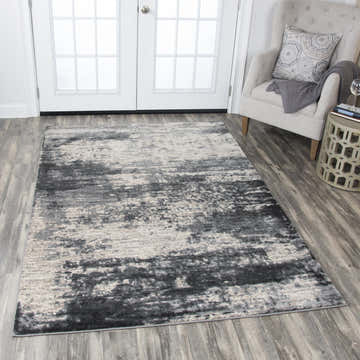 Living room scene with Rizzy PN6990 area rug in beige and gray, styled with a gray chair and wood floors. Roomscene-Rectangle