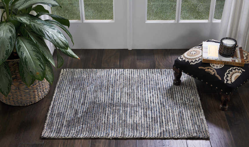 Entryway with Nourison Ellora Slate rug, dark wood floors, potted plant, and patterned ottoman near a bright window.