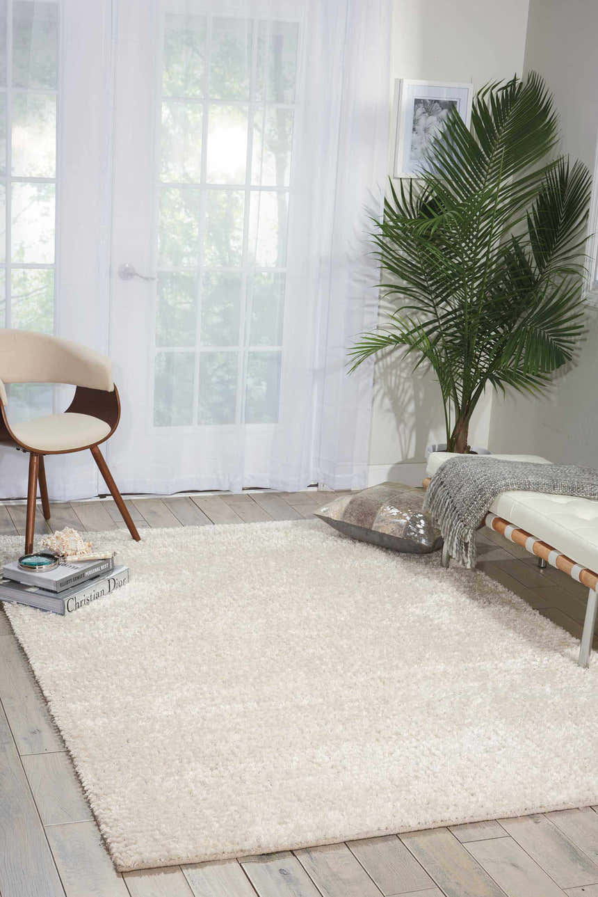Bright room scene with a Nourison Fantasia Snow Shag rug, white bench, palm tree, and light wood floors.