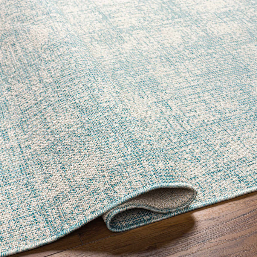 Close-up of the Rhea Area Rug showing its denim blue and natural gray woven texture on a wood floor. Fold