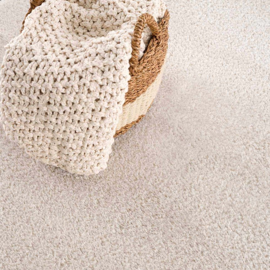 Close-up of the Velora Light Beige rug showing its soft, shag texture and a woven basket with a chunky knit blanket. Styleshot