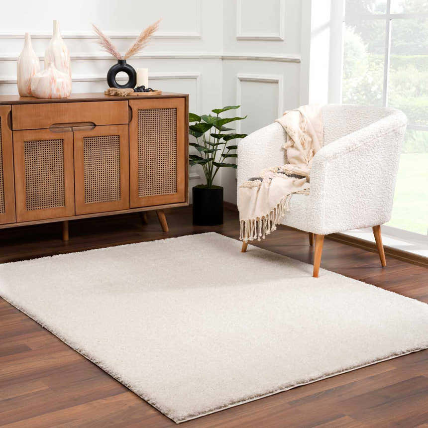 Living room scene with Velora Light Beige rug, wood cabinet, and white armchair. Modern minimalist style. Roomscene-Rectangle