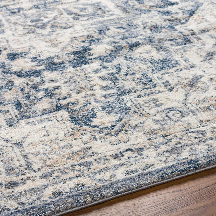 Close up of the Shotts Thick Luxe Rug, showing its traditional pattern in cream, tan, and dark blue on wood flooring. Texture