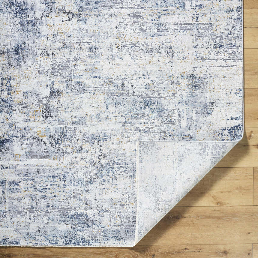 Close-up of the Hyman Area Rug showing its distressed pattern in camel, gray, and denim on a light wood floor. Fold