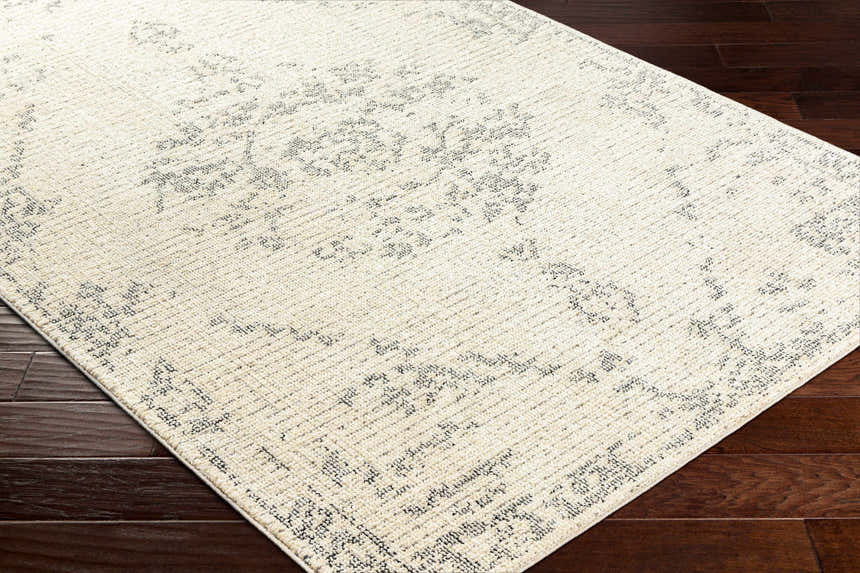Close-up of the Tait Area Rug in bone and cloud gray with a traditional, distressed pattern on dark wood floors. Corner