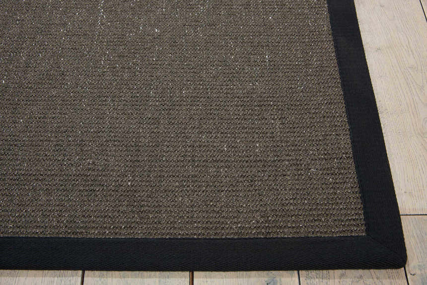 Close-up of the textured Michael Amini Brilliance Charcoal rug with a dark border on light wood floors.