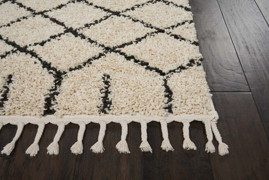 Close up of Nourison Moroccan Shag Cream Tribal rug showing shag texture, diamond pattern, and fringe detail on dark wood floor.