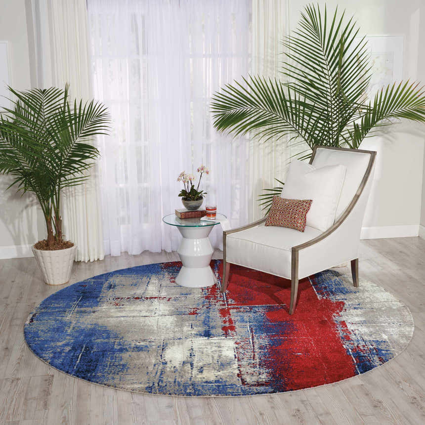 Living room scene with a round Nourison Twilight Multicolor rug, white chair, and palm trees. Modern style.