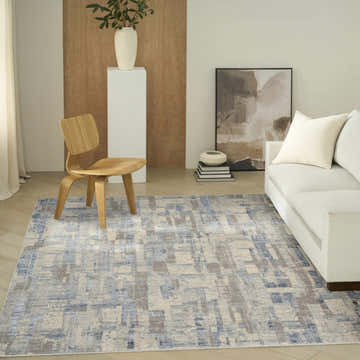 Living room scene with a blue beige Calvin Klein CK089 Drift area rug, white sofa, and wood chair. Modern style.