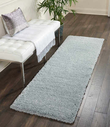 Entryway scene with a Nourison Malibu Shag Slate rug, white bench, silver pillow, and dark wood floors.