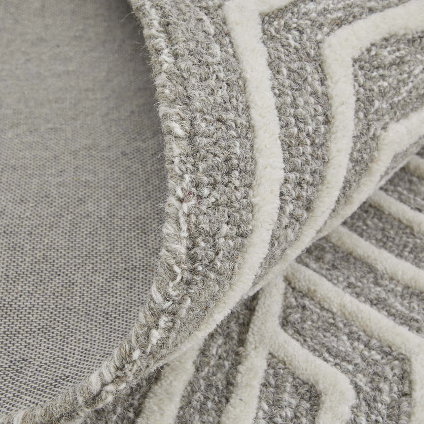 Close-up of the Feizy Lytton rug showing gray wool texture, ivory geometric pattern, and hand-tufted construction. Fold