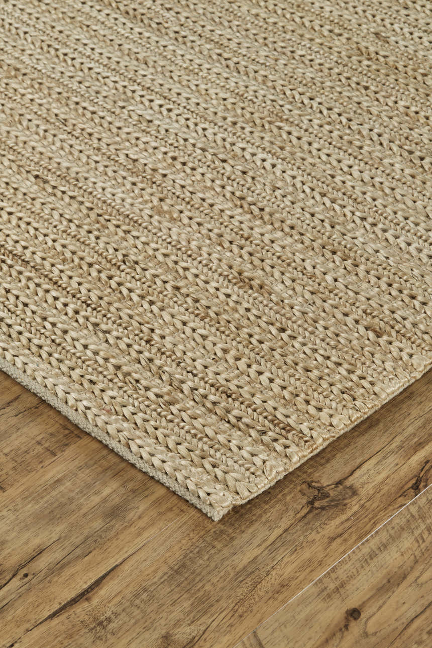 Close-up of the hand woven Feizy Kaelani rug. Tan, ivory, and taupe jute rug on a wood floor. Corner