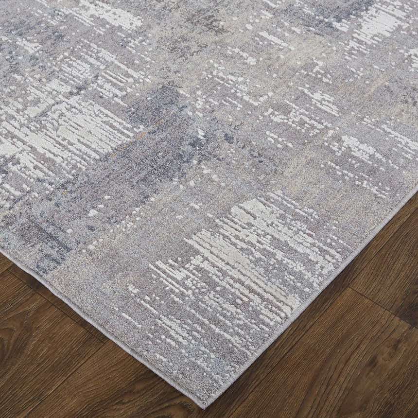 Close up of the Feizy Lennon rug in taupe, tan, and blue with an abstract pattern on a hardwood floor. Corner
