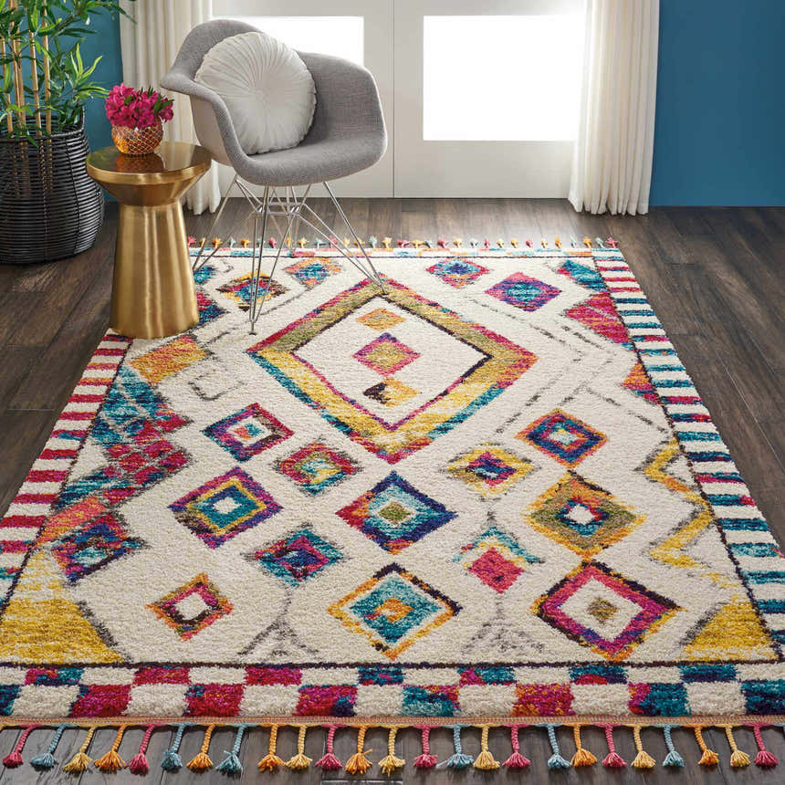 Living room scene with Nourison Nomad Ivory Multicolor Tribal rug, gray chair, gold accent table, and dark wood floors.