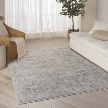 Living room scene with a DKNY Pure Shades Grey Vintage Indoor Area Rug, white sofa, and wicker chair.