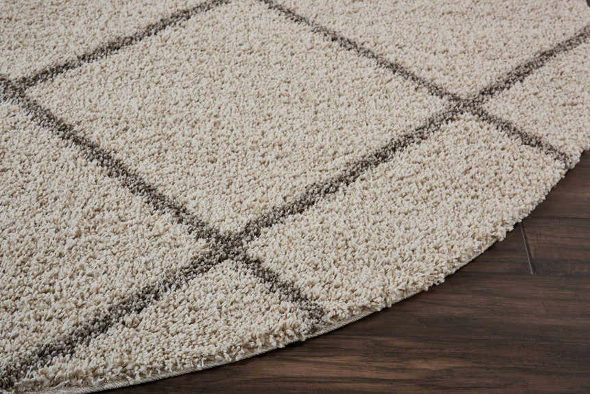 Close-up of the cream Nourison Brisbane shag rug with a geometric pattern on dark wood flooring. Soft texture.