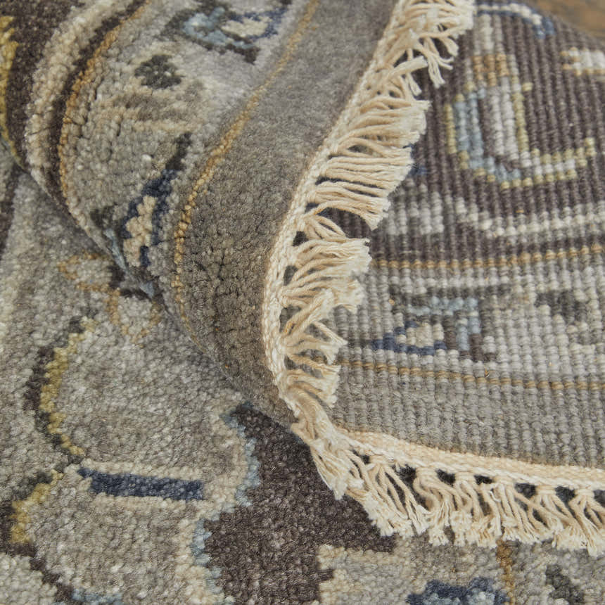 Close-up of the Feizy Ustad rug. Traditional Persian design in gray, taupe, and blue. Hand-knotted wool rug with fringe detail. Fold