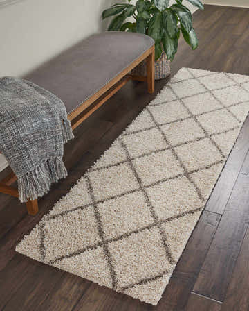 Hallway scene with a Nourison Brisbane Cream Shag rug runner, gray bench, throw blanket, dark wood floors, and potted plant.