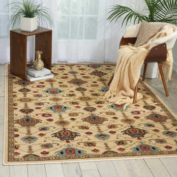 Cozy room scene with a Nourison Delano Ivory rug, wood chair with throw, side table, and light wood floors.