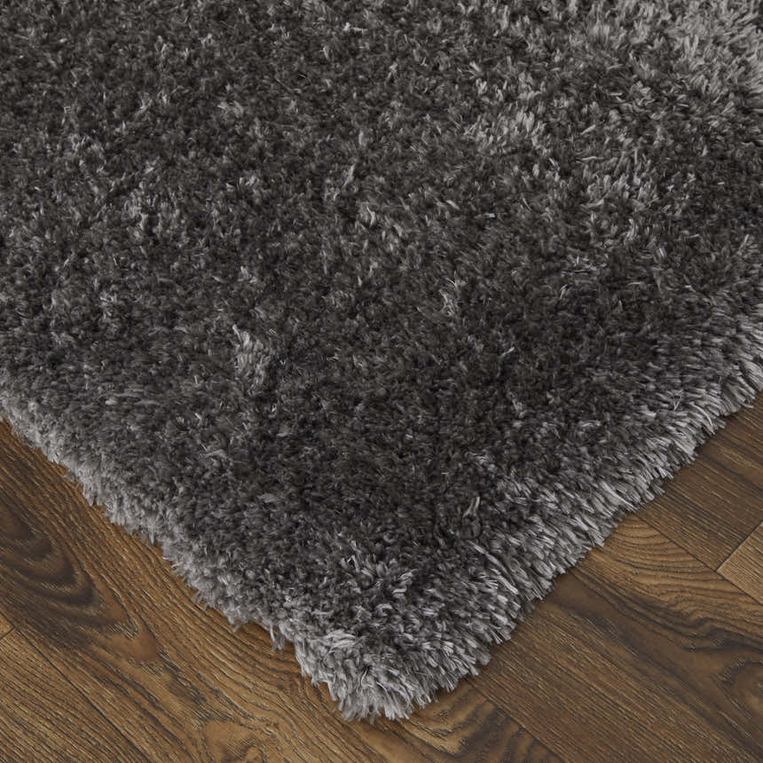 Close-up of the plush texture and corner of a gray Feizy Darian area rug on a wood floor. Corner