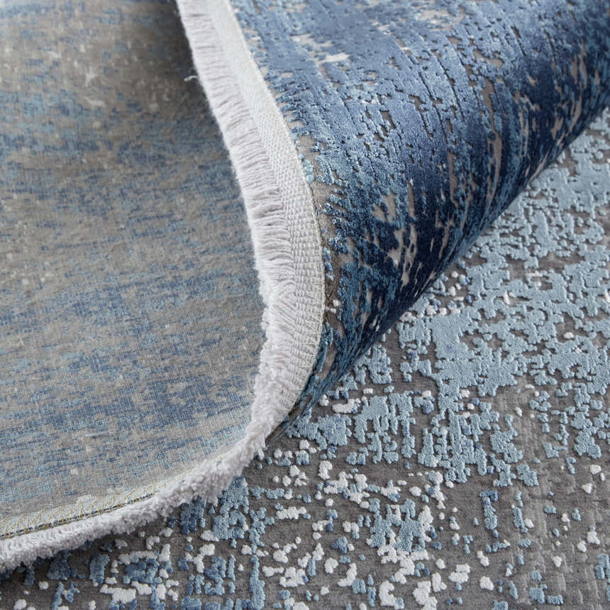 Close up of the Feizy Cadiz Modern Abstract rug in blue, gray, and silver. Features a textured abstract pattern and fringe detail. Fold