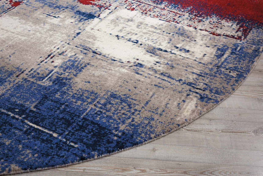 Close up of a round Nourison Twilight Multicolor rug showing blue, red, gray and white abstract pattern on wood floor.