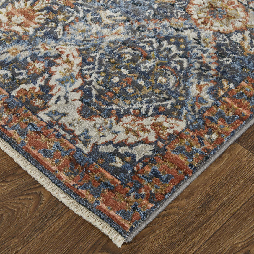 Close up of Feizy Kaia rug showing its blue, orange, and ivory floral pattern and texture on a wood floor. Corner