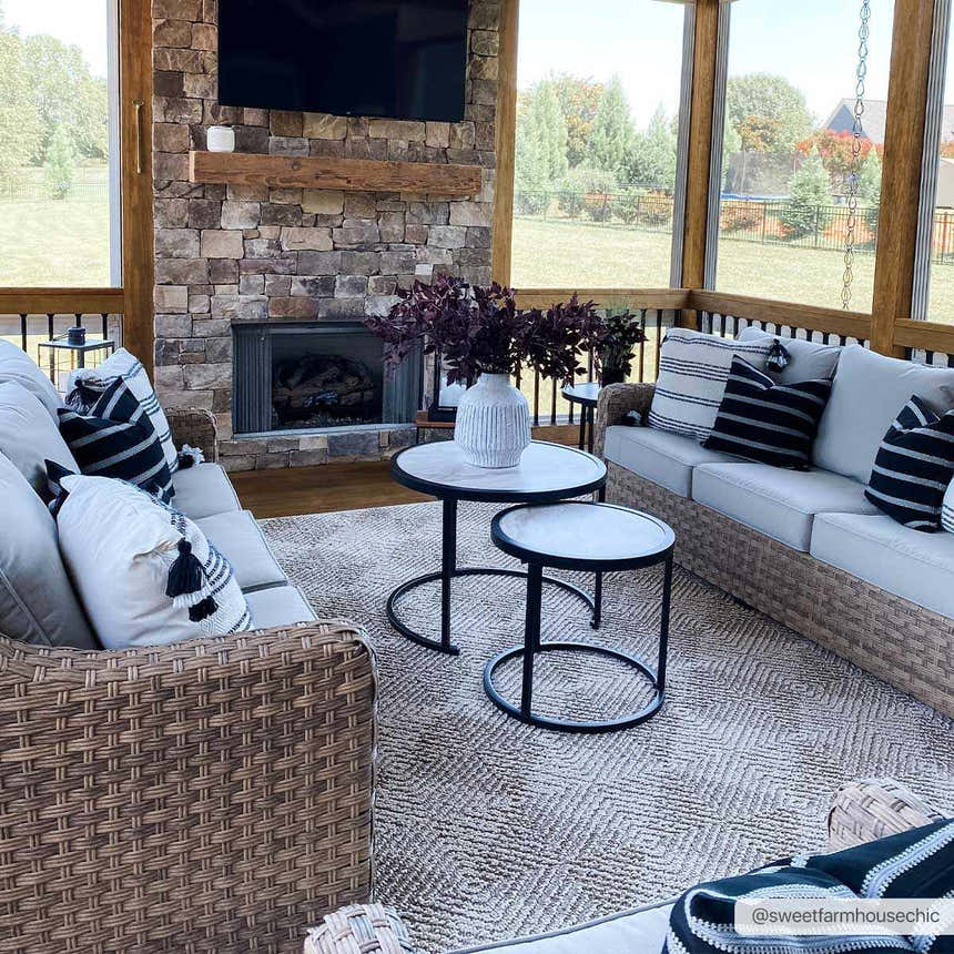 Sunroom with stone fireplace featuring Broox Beige Area Rug, wicker sofas, and black and white accents. Roomscene-Rectangle