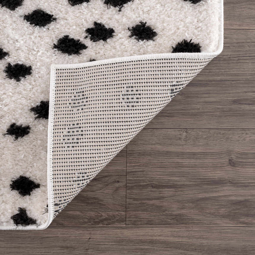 Close-up of the Cansu Black & White Dotted Area Rug showing its shag texture and black dotted pattern on an off-white base. Fold