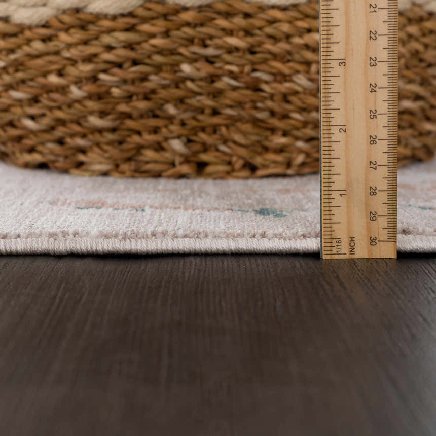 Close-up of the cream Danlugan Area Rug showing pile height with a ruler and a woven basket on a dark wood floor. Pile