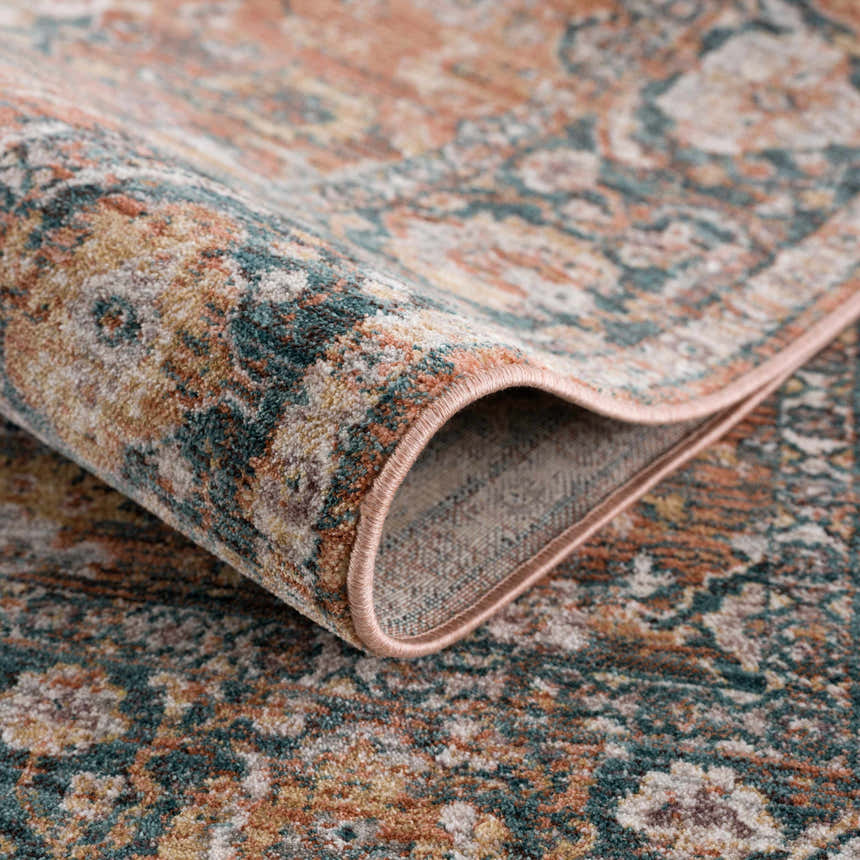 Close-up of the Mele Area Rug showing its traditional pattern, burnt orange, olive, and beige colors, and soft, textured pile. Fold