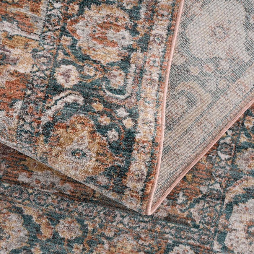 Close-up of the Mele Area Rug showcasing its traditional pattern in bone, burnt orange, and olive tones. Machine woven texture. Fold