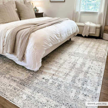 Bedroom scene with a bone and gray Cosma Area Rug under a bed with white linens and neutral pillows. Roomscene-Rectangle