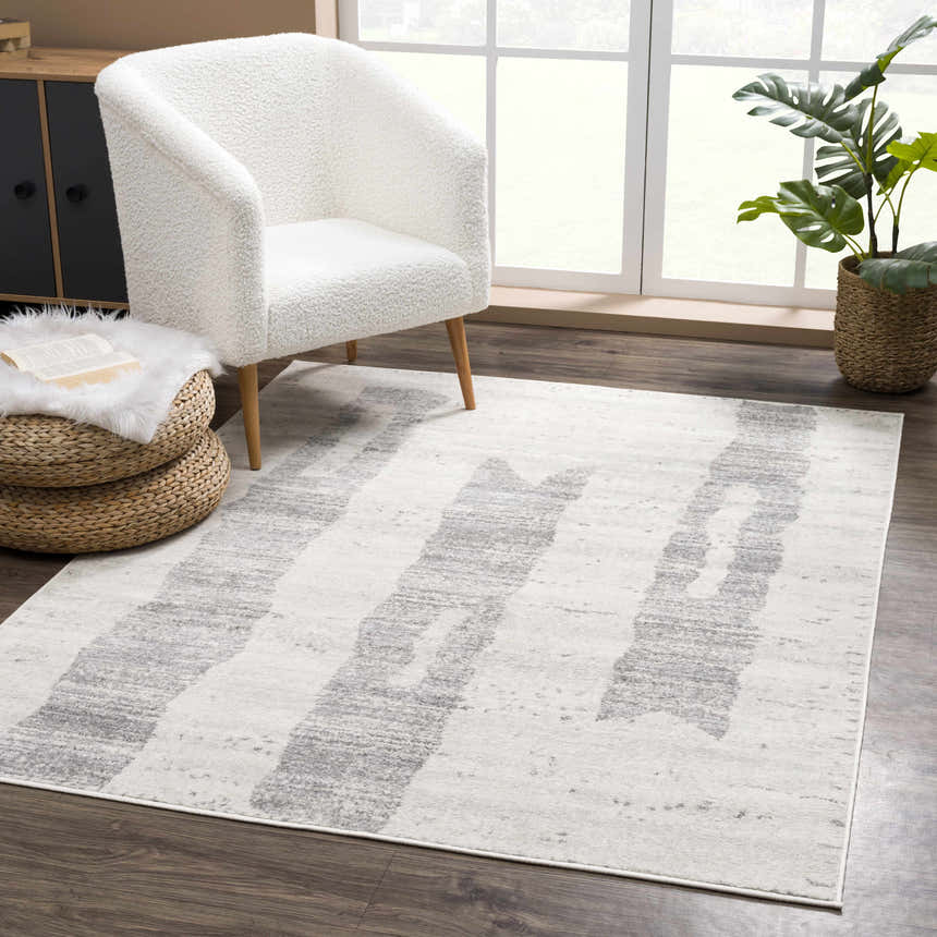 Living room scene with a Tigria Ivory 2316 area rug, white chair, woven ottoman, and potted plant by a window. Roomscene-Rectangle