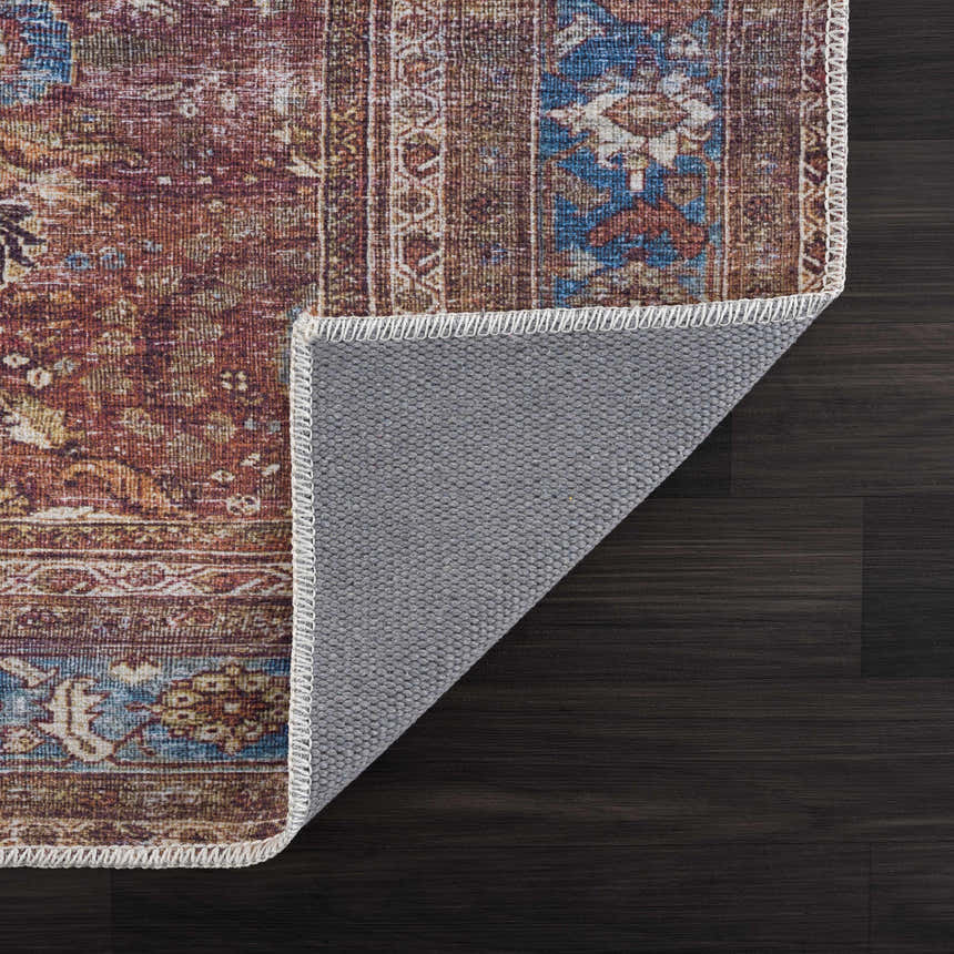 Close-up of the Rust Baki Washable Area Rug showing its rust, orange, and blue traditional Persian design and gray backing. Fold