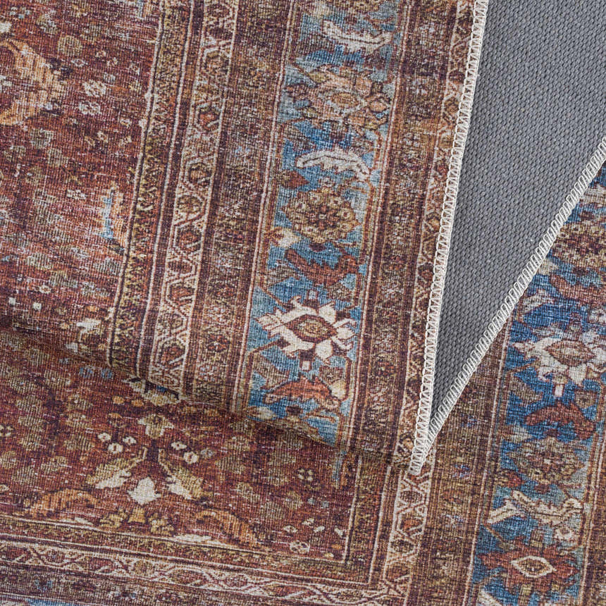 Close-up of the Rust Baki Traditional Washable Area Rug showing its Persian-style pattern and rust, blue, and off-white colors. Fold