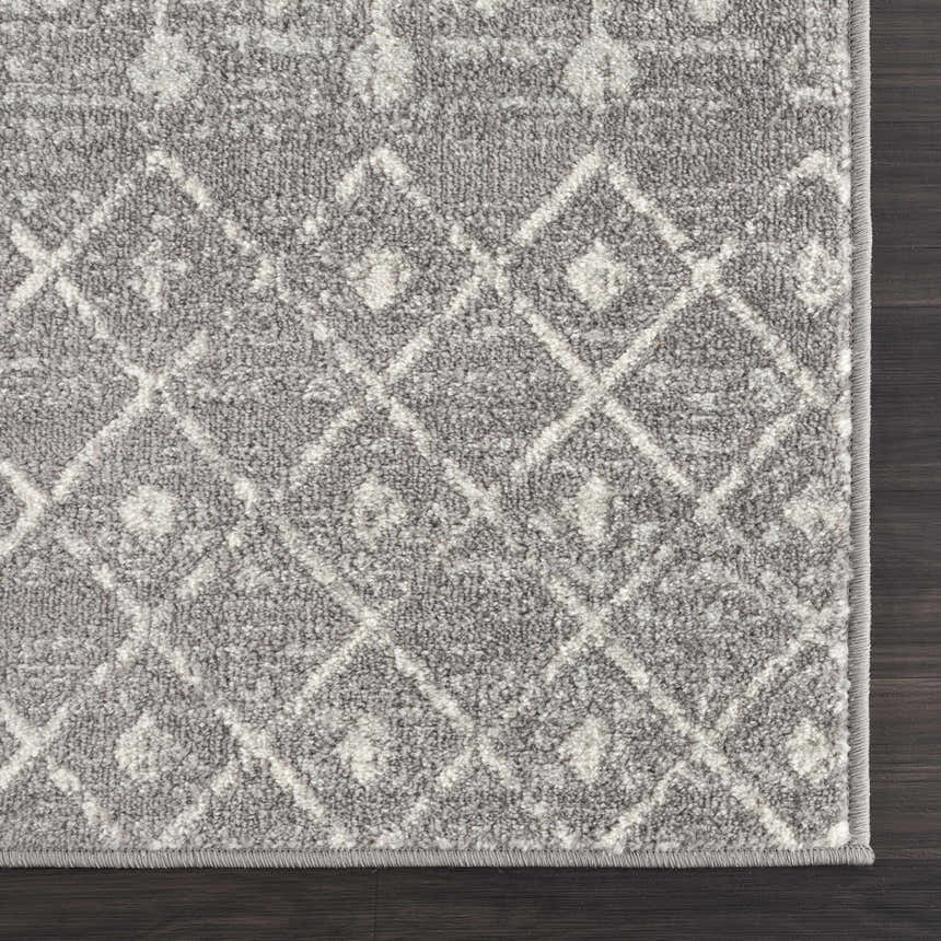 Close-up of the Marash KMRSH-4607 area rug. Dark gray rug with an ivory diamond pattern on a dark wood floor. Corner
