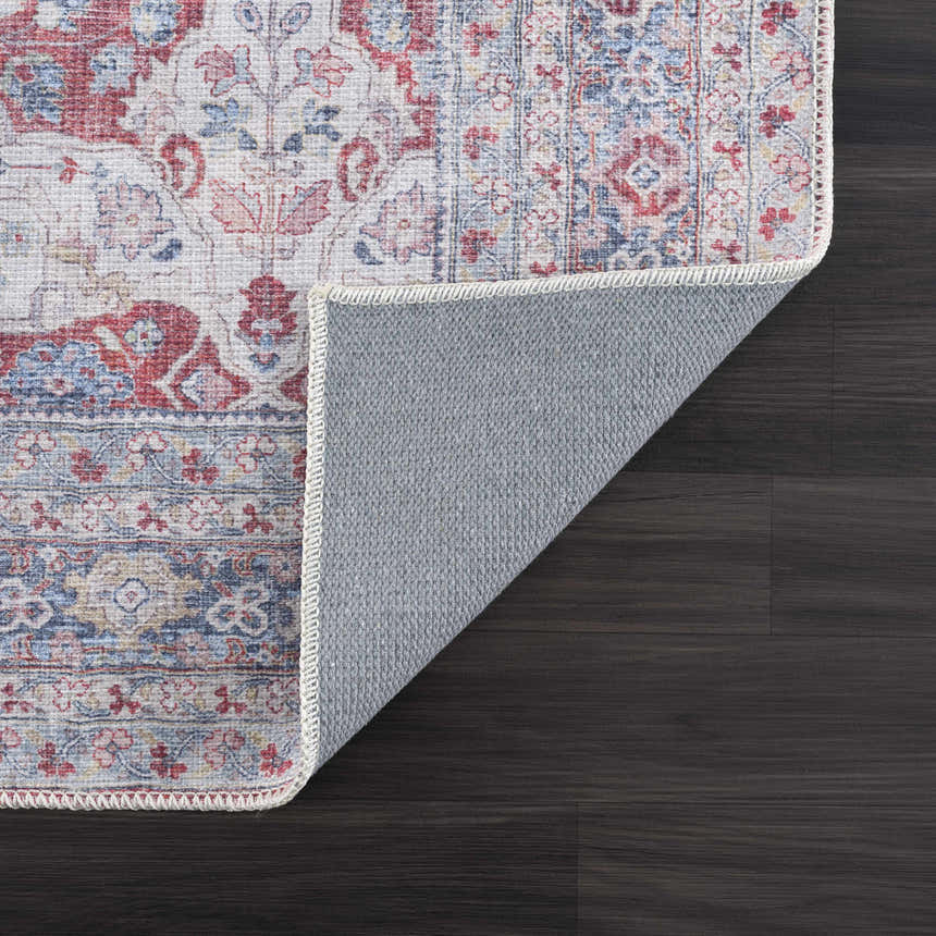 Close-up of the Rust Goma Vintage Area Rug showing blush, red, and blue floral pattern and gray backing on dark wood floor. Fold