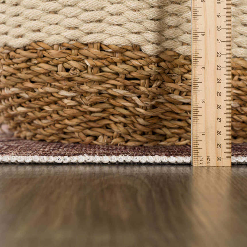 Close-up of the Nadie Beige Medallion Area Rug showing the rug's thickness with a ruler and a basket. Pile