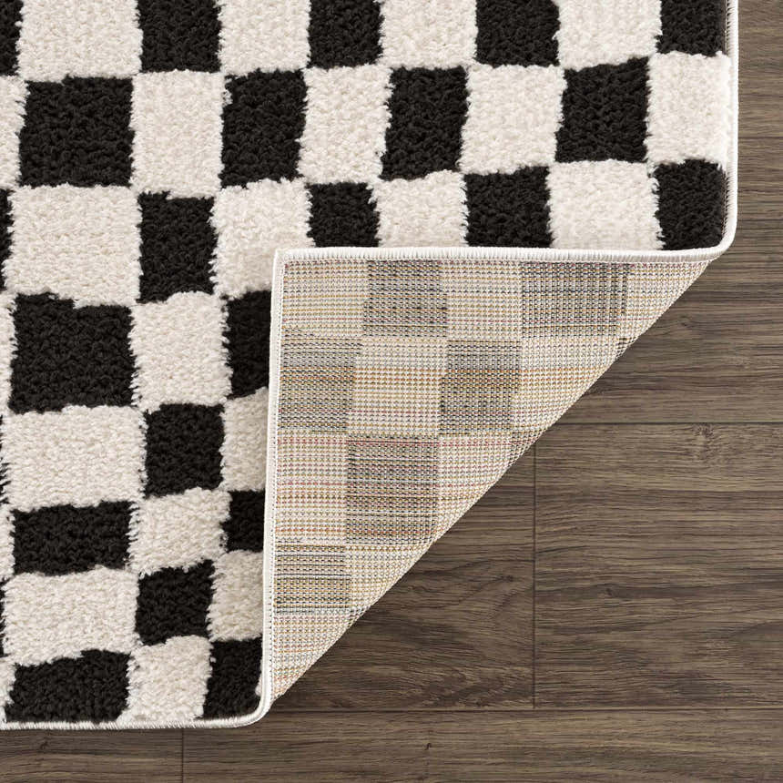 Close-up of Lajos Black & White Checkered Plush Rug showing the plush texture, checker pattern, and rug backing. Fold