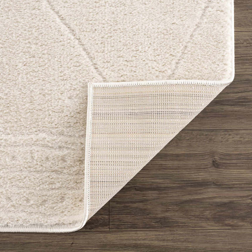 Close up of Keone Ivory Area Rug showing the plush pile, geometric pattern, and backing on dark wood floors. Fold