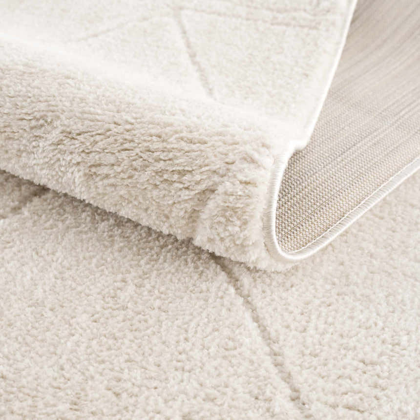 Close-up of the plush, ivory Keone Area Rug, showing its soft texture, geometric pattern, and durable backing. Fold