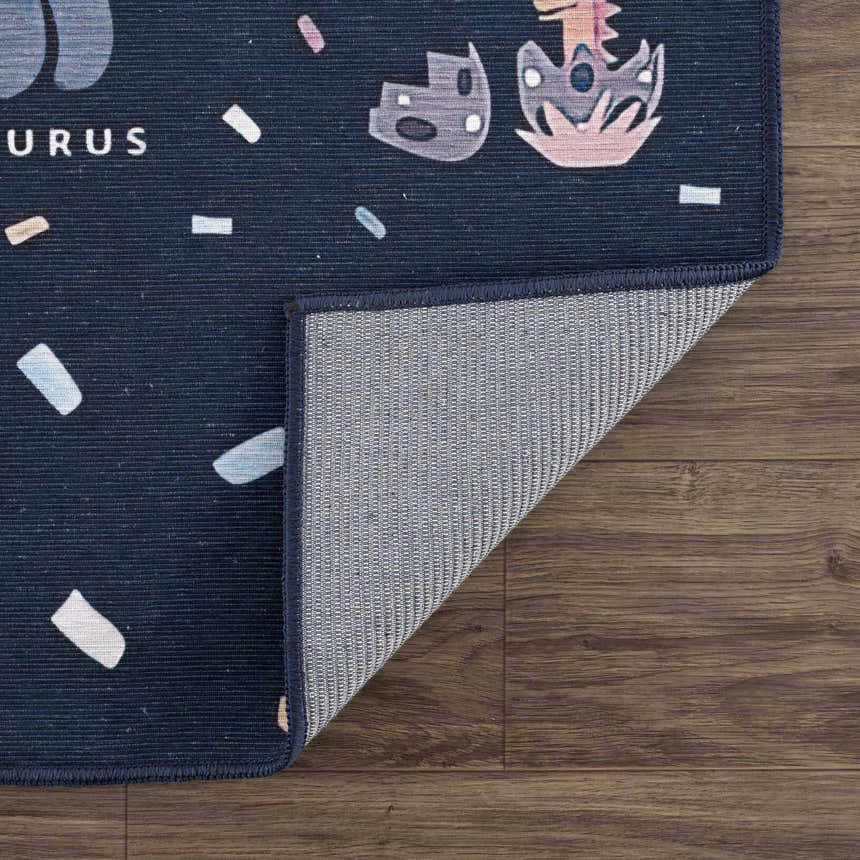 Close-up of the Milne Navy Dinosaur Washable Kids Rug showing its navy blue color, dinosaur pattern, and the rug's backing. Fold