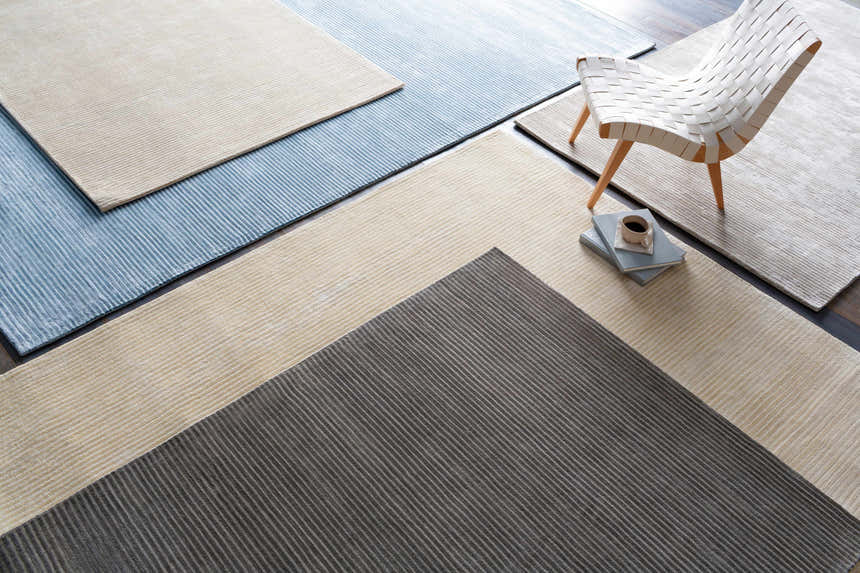Overhead view of Ahmeek Area Rug samples in gray, beige, and blue with linear texture, styled with a chair and coffee. Styleshot