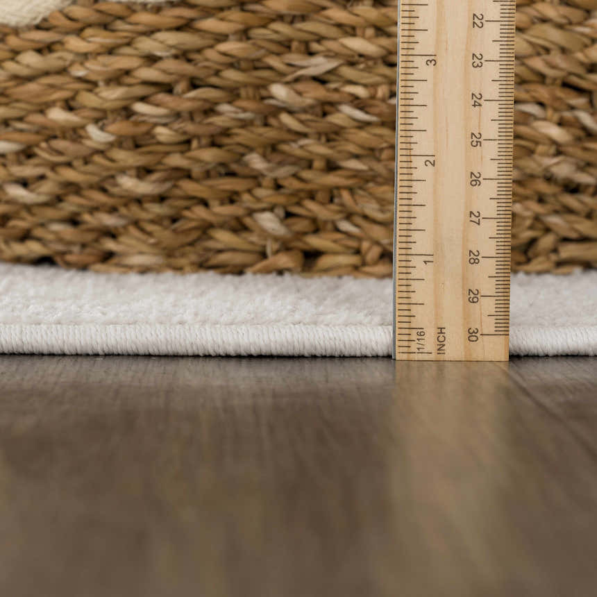 Close-up of the Senekal 3D Outdoor Area Rug showing its off-white pile height with a ruler and a woven basket. Pile