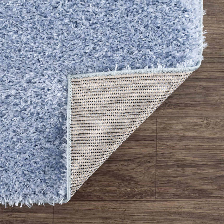 Close-up of the Faina Solid Aqua Shag Washable Area Rug showing its soft, plush texture and durable backing on a wood floor. Fold