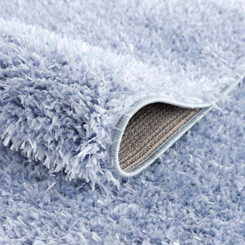 Close-up of the plush texture and backing of the Faina Solid Aqua Shag Washable Area Rug. Fold