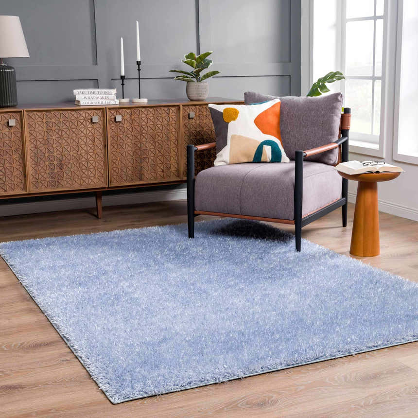 Living room scene with a Faina Solid Aqua Shag rug, gray chair, wood cabinet, and light wood floors. Roomscene-Rectangle